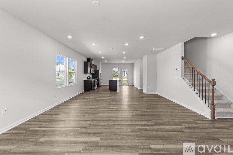 A spacious room with wooden flooring and a staircase on the right side.