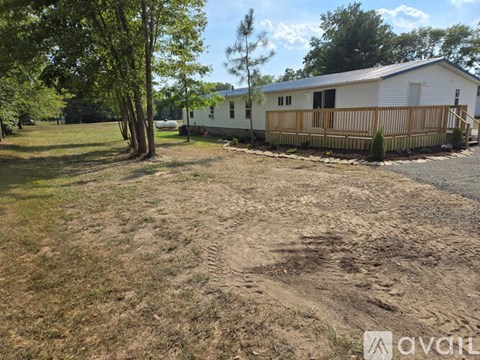 A white mobile home with a wooden deck and a tree in front.