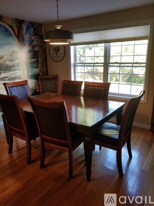 A wooden dining table with chairs and a hanging light fixture in a room with a large window.