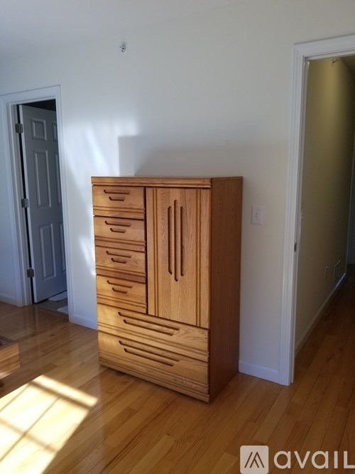 A wooden cabinet with drawers is in a room with a white wall and a door.