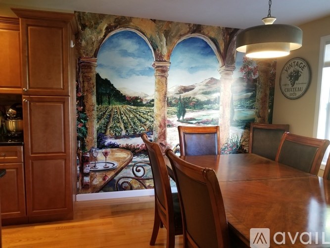 A dining room with a large painting of a vineyard on the wall.