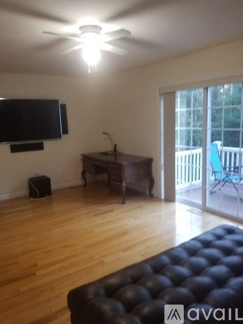 A living room with a black leather sofa and a flat screen TV mounted on the wall.