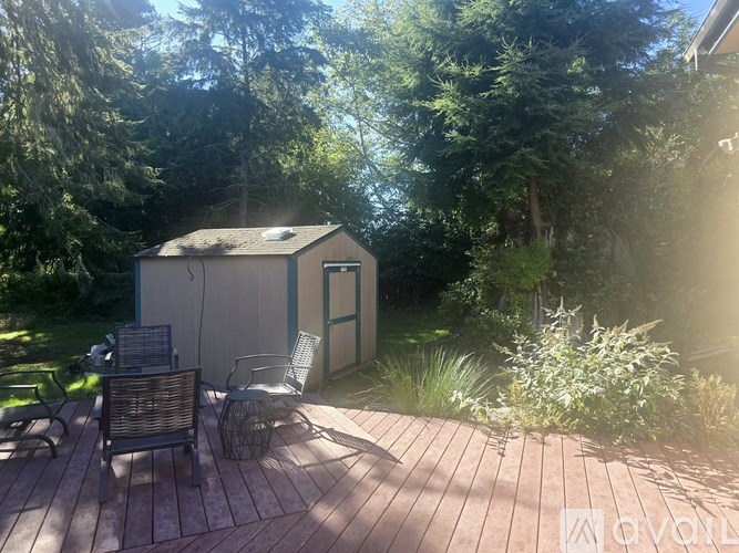 A wooden deck with a chair and a table in front of a small house surrounded by trees.