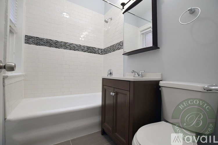 A white tiled bathroom with a white bathtub, a toilet, and a mirror.