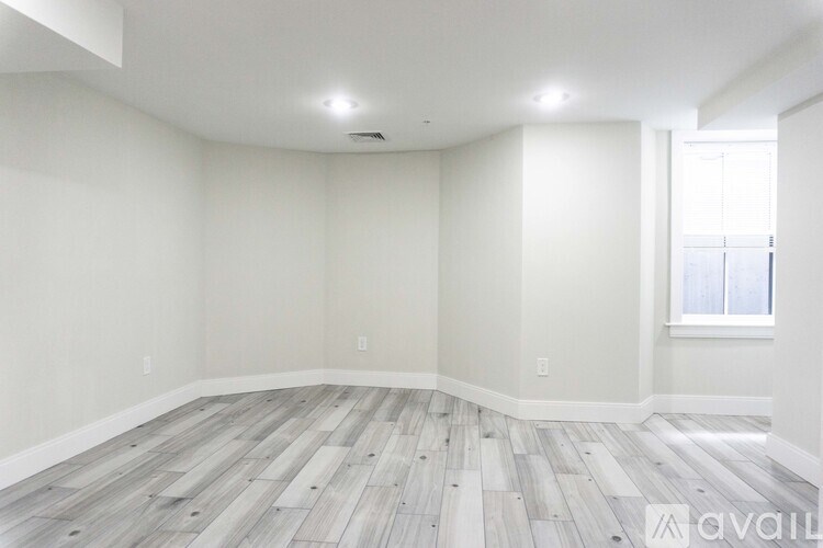 A spacious room with wooden flooring and white walls.