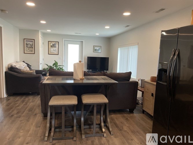 A modern kitchen with a refrigerator, a table with two chairs, and a living room with a couch and a television.