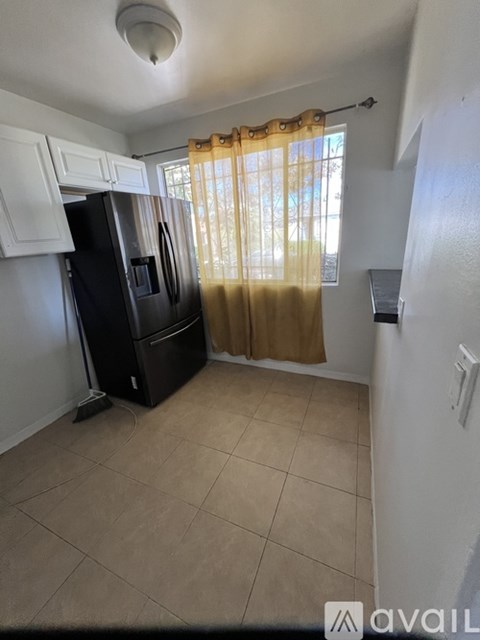 A kitchen with a black fridge and a window with curtains.