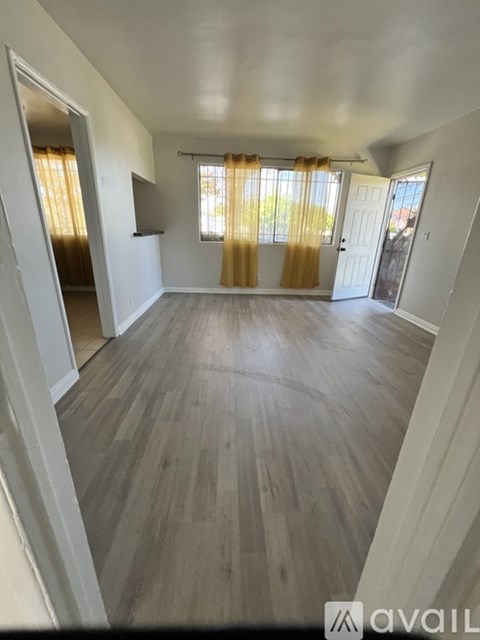 A spacious room with wooden flooring and a window with yellow curtains.
