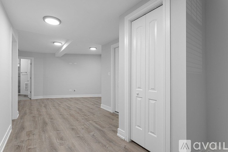 A spacious room with a white door and light wooden flooring.