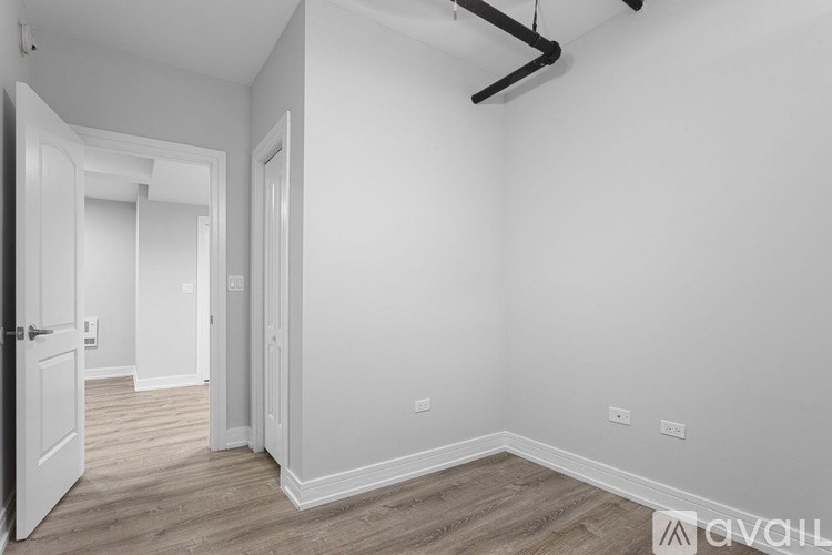 A room with white walls and wooden flooring, with a door on the left and a window on the right.