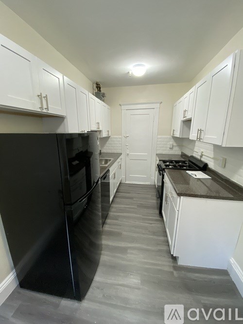 A kitchen with white cabinets and a black refrigerator.
