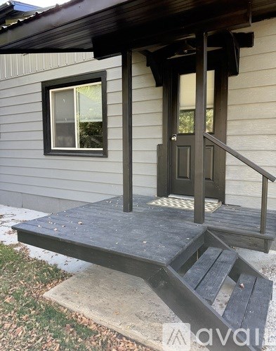 A wooden porch with a black door and steps leading to it.