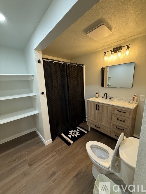 A bathroom with a toilet, sink, mirror, and shelves.