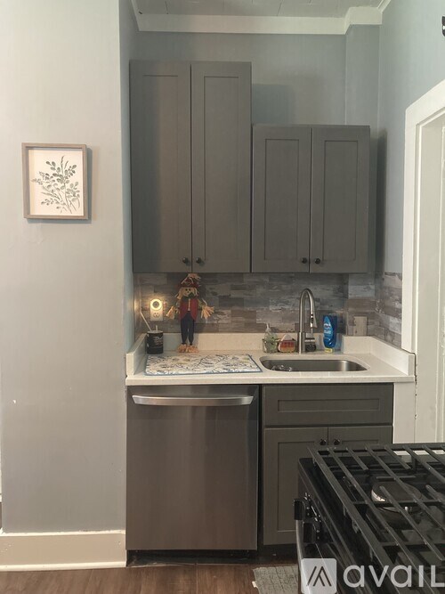 A kitchen with a stainless steel dishwasher and grey cabinets.