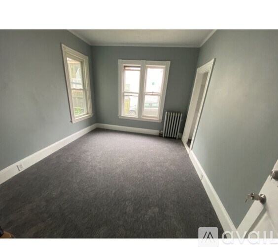 A room with a grey carpet and a window with white curtains.