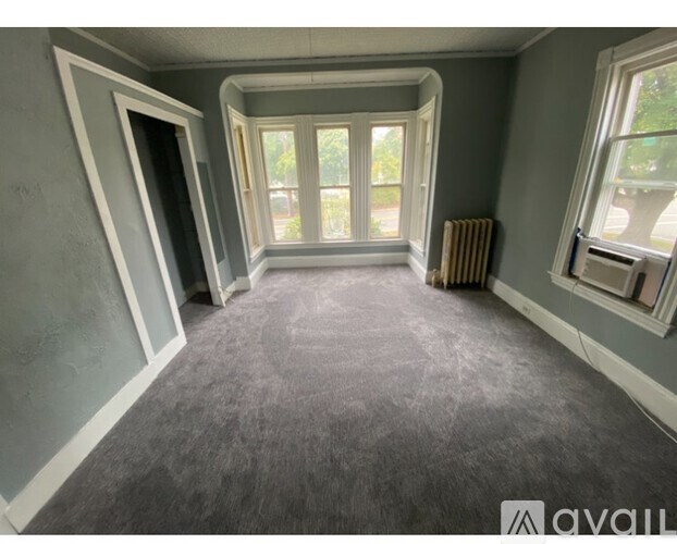 A room with grey carpet and a window overlooking a street.
