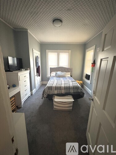 A room with grey carpet and a window showing a tree outside.