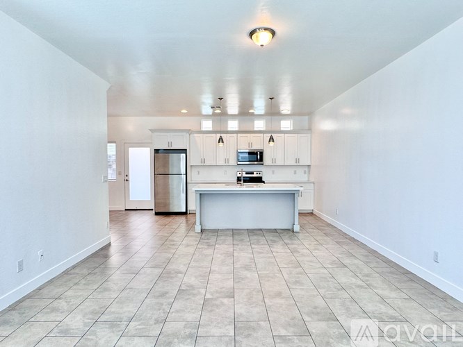 A kitchen with white cabinets and appliances in a large empty room.