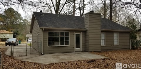 A small house with a grey roof and a grey wall is surrounded by a fence.