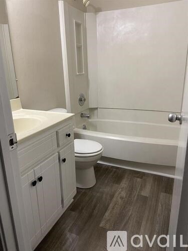 A white bathroom with wood flooring and a white tub.