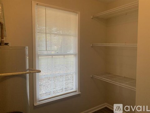 A room with a window covered by white blinds and three empty shelves.