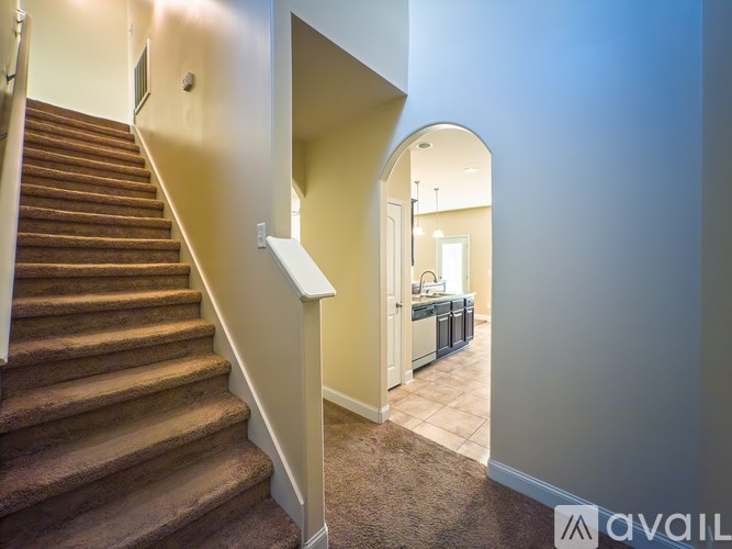A staircase with a carpeted floor and a white railing leads to a kitchen area.