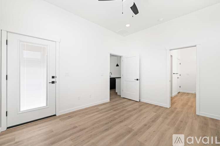 A room with white walls and wooden flooring, with three doors and a ceiling fan.