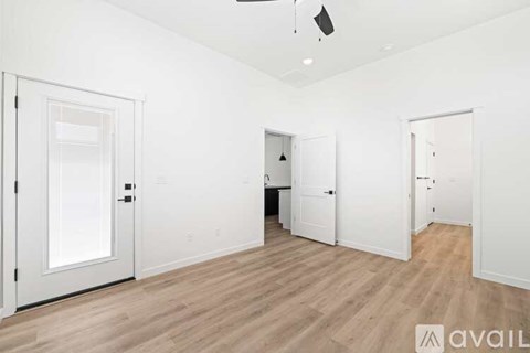 A room with white walls and wooden flooring, with three doors and a ceiling fan.