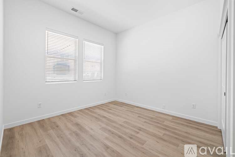 A room with wooden flooring and two windows.