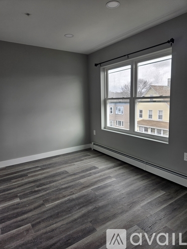 A room with grey walls and a window showing a view of buildings outside.