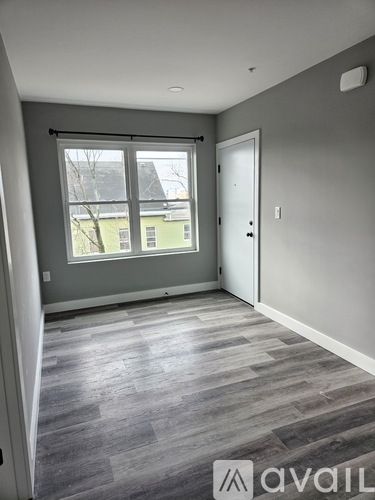 A room with grey flooring and a window overlooking a green building.