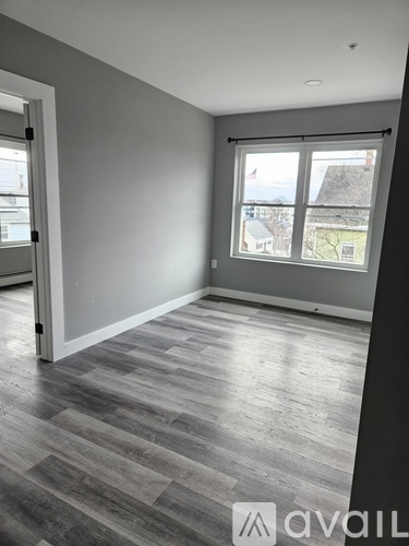 A room with grey walls and wooden flooring with a window showing a view of a house and trees.