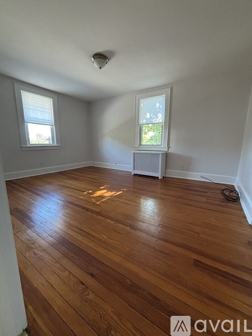 A room with wooden flooring and two windows.