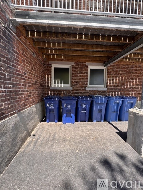 A row of blue bins are placed in front of a brick wall.