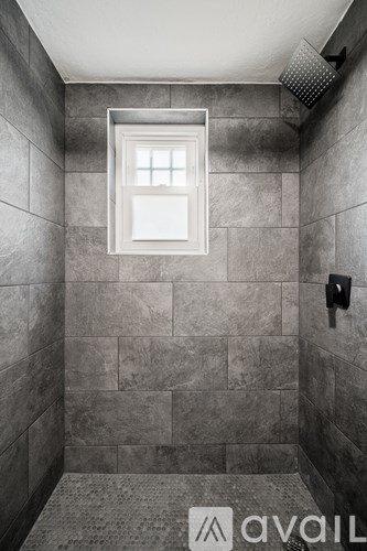 A bathroom with grey tiles and a window.