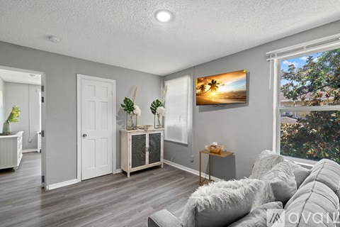 A living room with a grey couch and a painting of a beach scene on the wall.