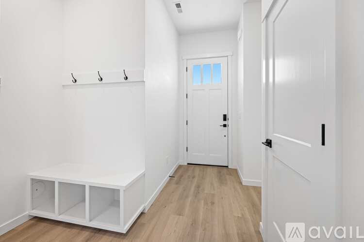 A white hallway with a bench and three hooks on the wall.