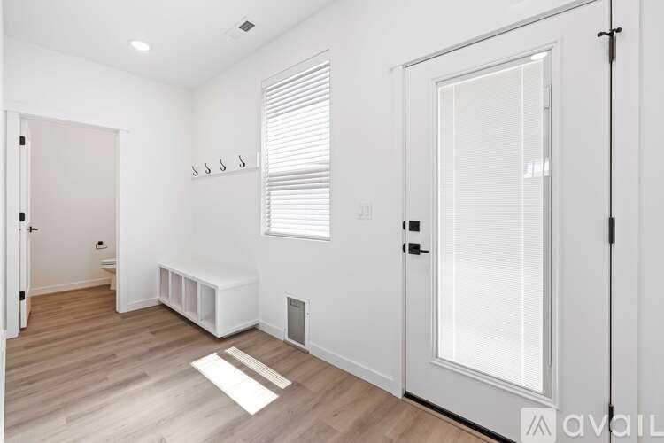 A room with a white door, window with blinds, and a white bench.