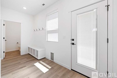 A room with a white door, window with blinds, and a white bench.