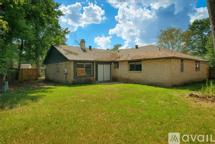 A house with a brown roof and a white door is surrounded by green grass and trees.