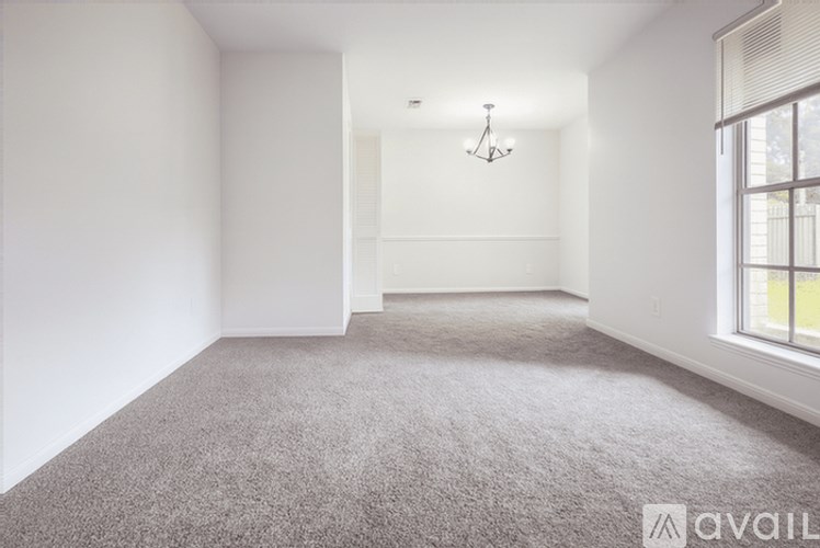 A spacious room with a grey carpet and a chandelier hanging from the ceiling.