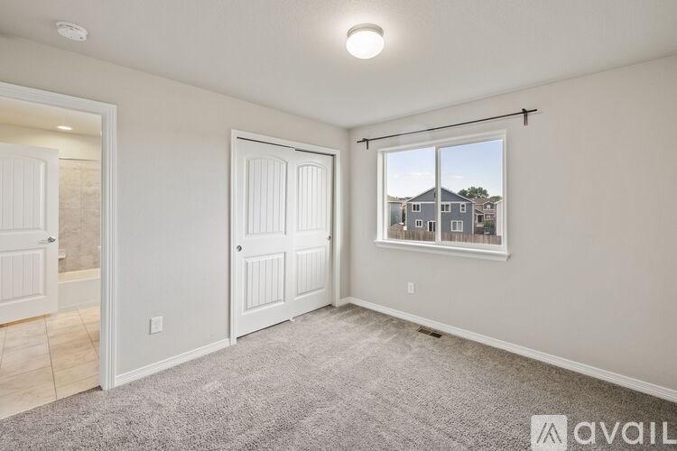 A room with a carpeted floor and a window showing a house across the street.