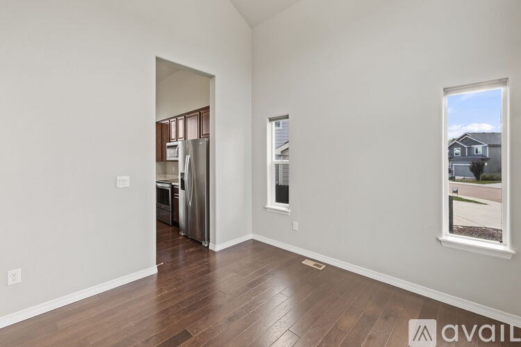 A room with wooden flooring and a window showing a view of a house.
