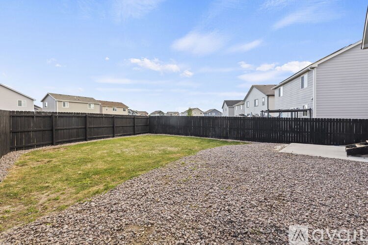 A gravel driveway leads to a black fence and houses in the background.
