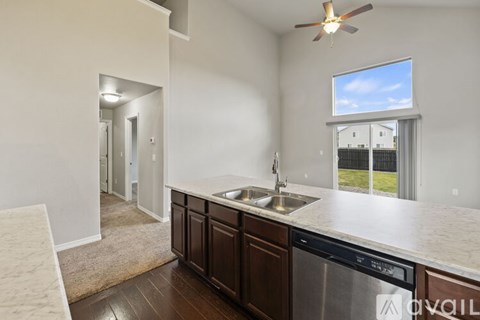 A kitchen with a stainless steel dishwasher and a window overlooking a fence.