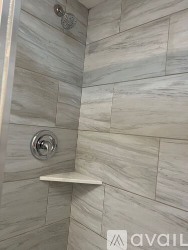 A shower area with a white shelf and a silver shower head.
