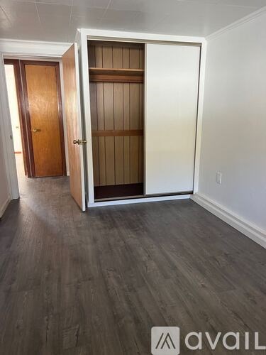 A room with a wooden floor and a white wall with a door and a closet.