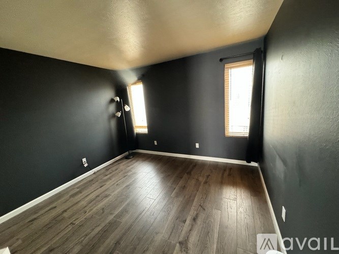 A room with wooden flooring and two windows.
