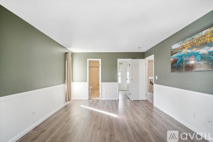 A room with wooden floors and white walls, with a painting on the wall and a door in the middle of the room.