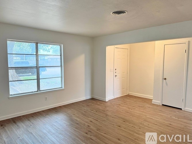 A room with wooden floors and white walls, featuring a window with a view of a tree and a car, and two white doors.